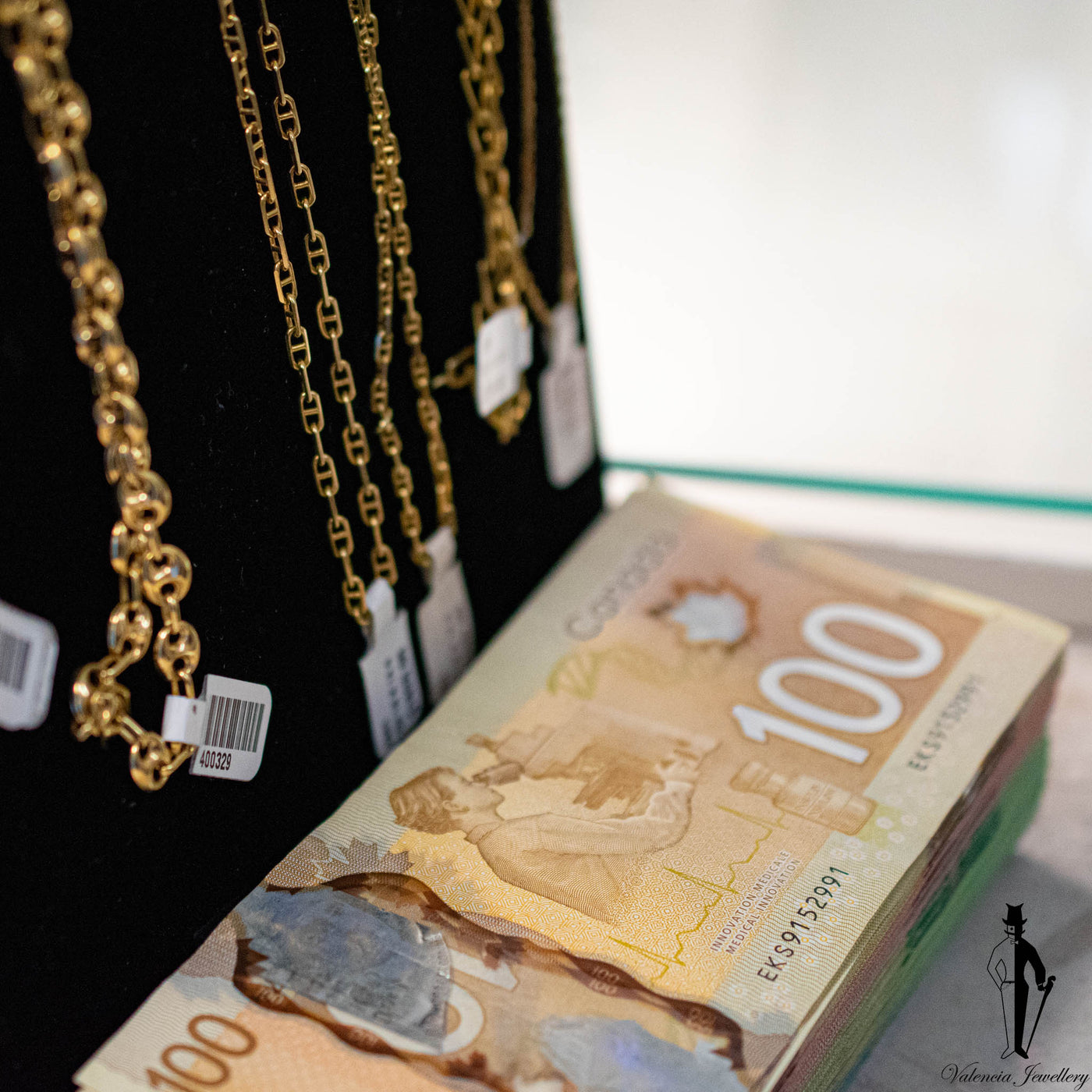 A stack of Canadian 100 dollar bills beside gold chains